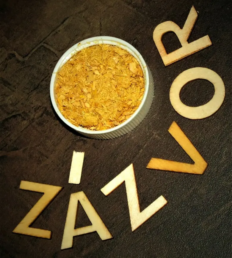 Sušený zázvor v misce s dřevěnými písmeny ZÁZVOR na tmavém povrchu.