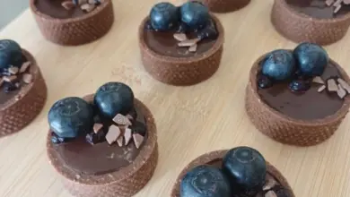 Čokoládové tartlety s malinami na dřevěném podkladu.