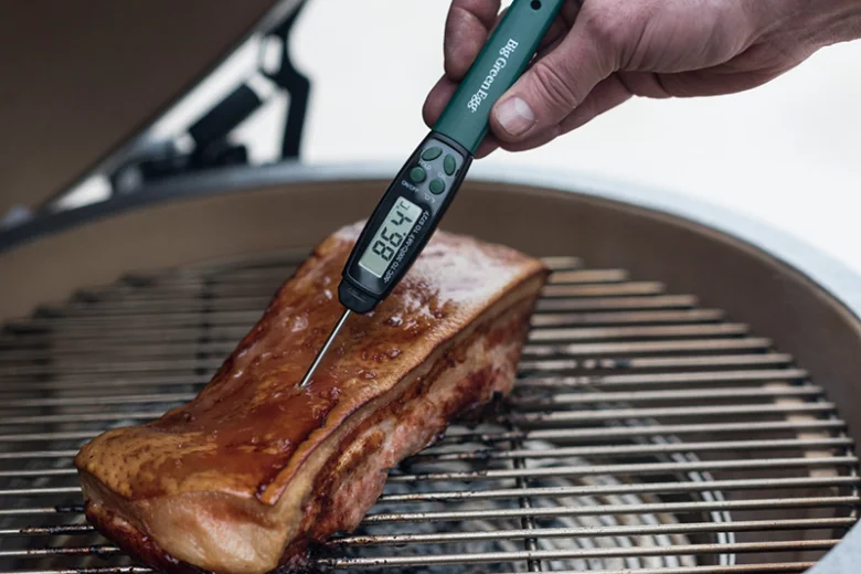 Digitální teploměr měří teplotu vepřového masa na grilu.