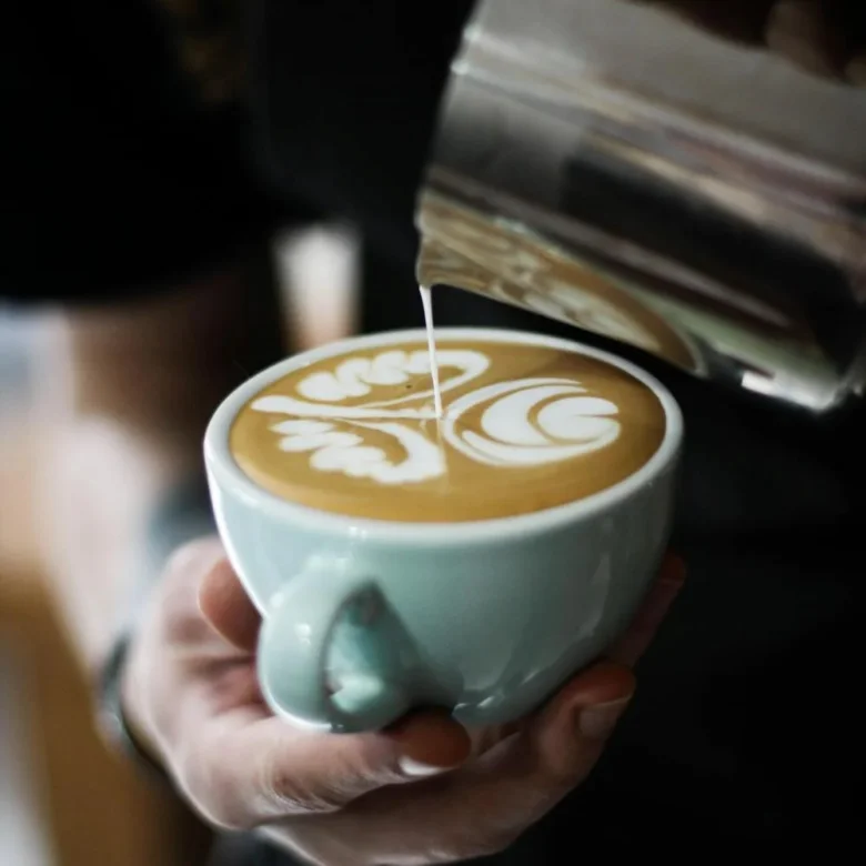 Barista nalévá mléko do kávy pro vytvoření latte art.
