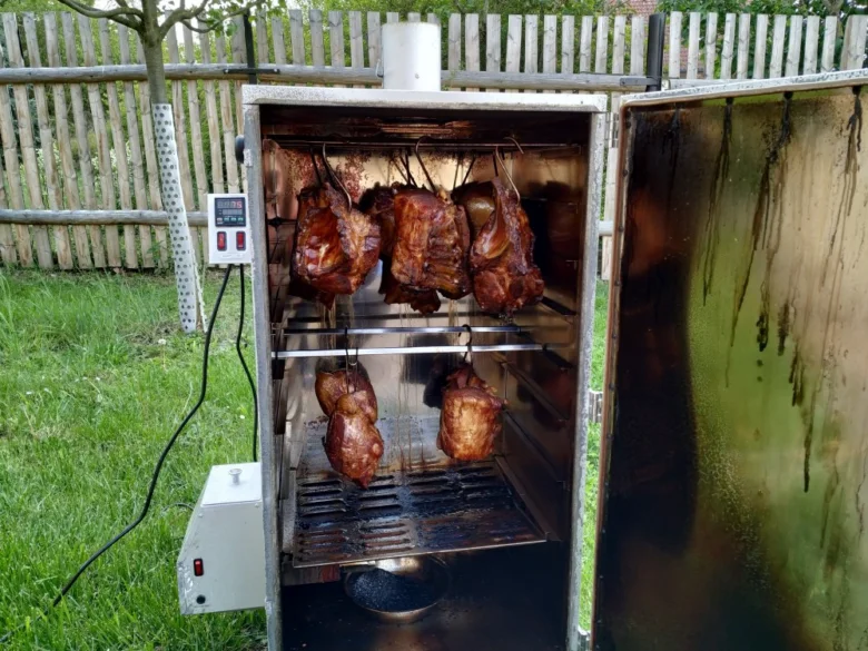 Uzené maso v elektrickém kouři venku s viditelným dýmem.