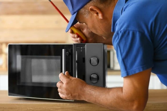Technik opravuje mikrovlnnou troubu s otevřenou dveřmi.