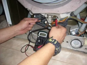 Ručník s multimetrem kontroluje elektrické součástky v pračce při opravě.