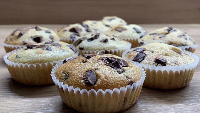 Svěžě upečené muffiny s čokoládovými kousky na dřevěném povrchu.