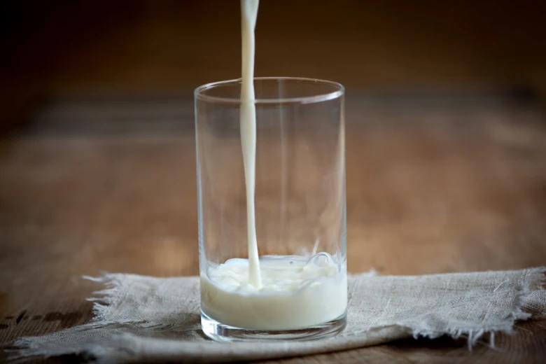 Bílá tekutina se nalévá do sklenice na ubrusu.
