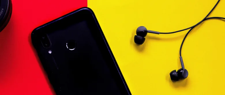 Černý chytrý telefon s bezdrátovými sluchátky na žlutém pozadí.