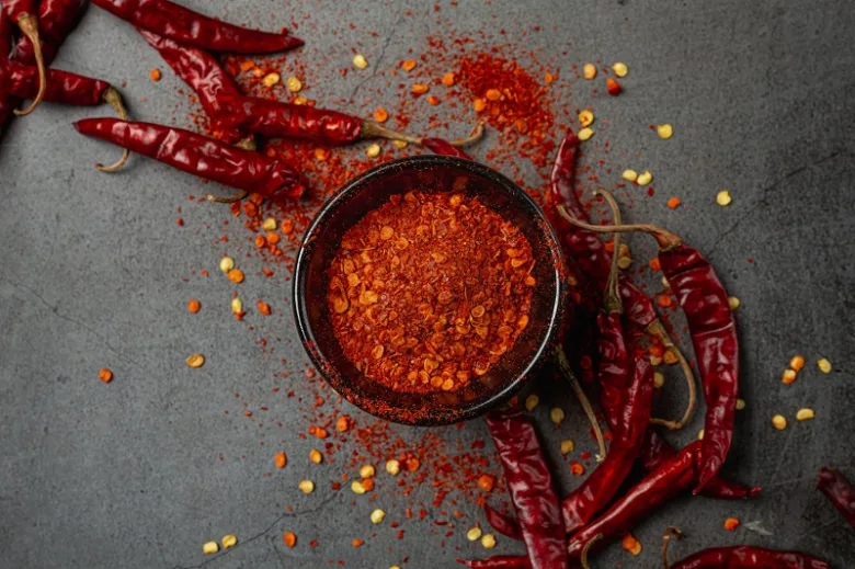 Sušené červené chilli papričky s mletou omáčkou na tmavém povrchu.