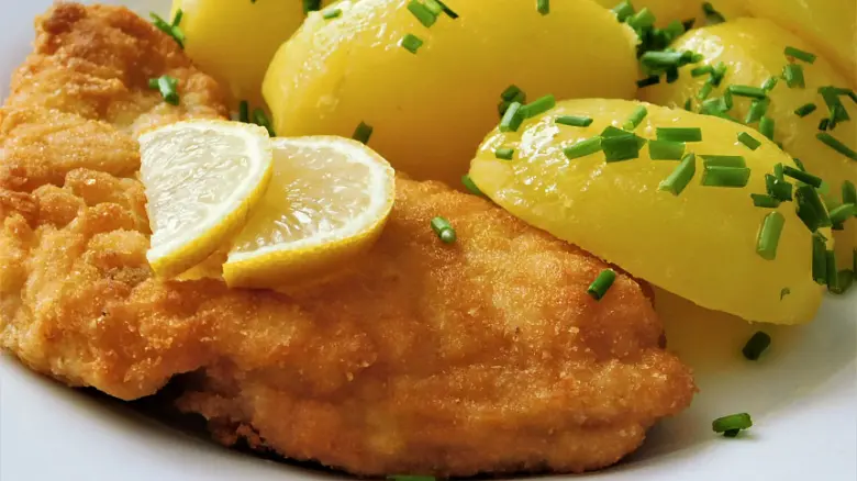 Smažený řízek s citronem, bramborami a nasekanou petrželkou.