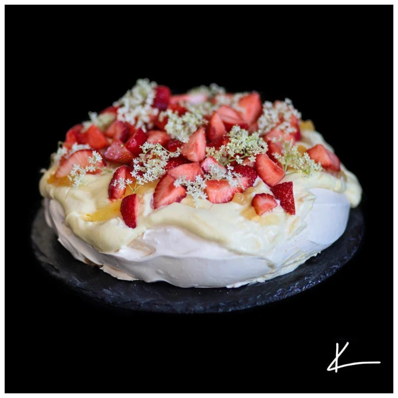 Pavlova dezert s jahodami na tmavém podstavci.