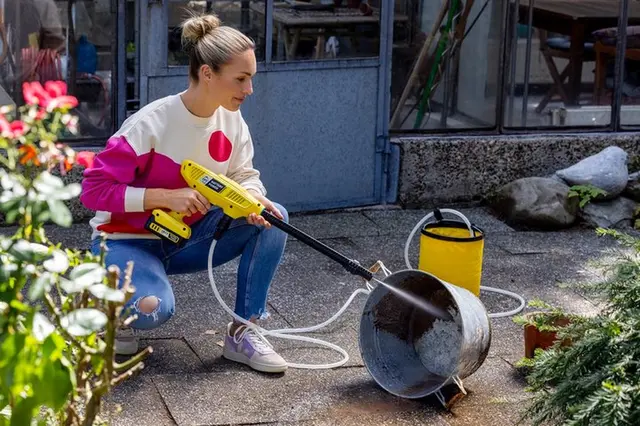 Žena v zahradě zavlažuje rostliny hadicí z kbelíku.