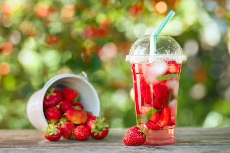 Domácí limonáda ze čerstvých jahod s mátou a ledem v průhledné sklenici na venkovním stole.