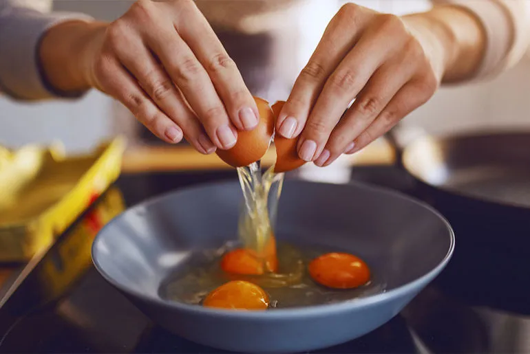 Ruce kladou vejce do misky s žloutkem a bílkem.