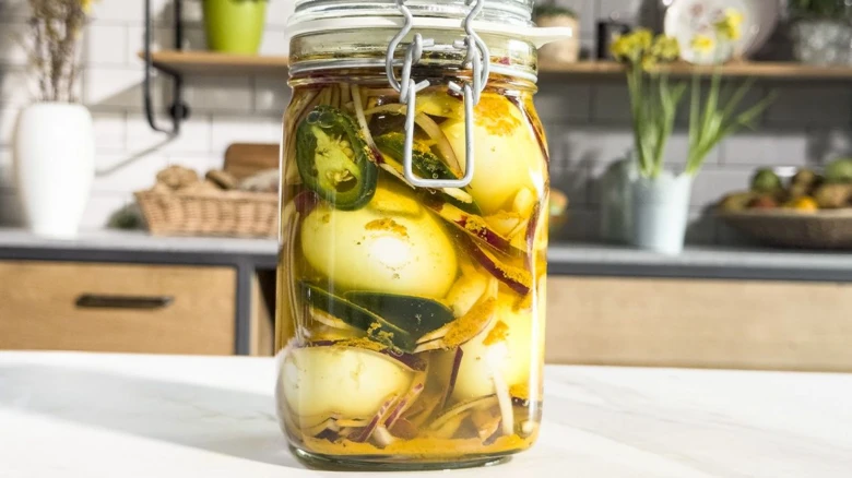 Sklenice nakládaných vajec s chilli a kořením na kuchyňské desce.