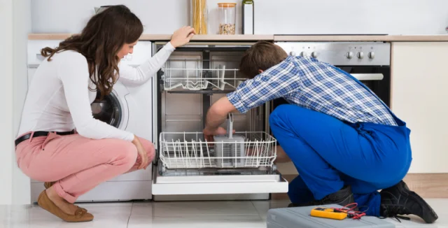 Technik opravuje myčku v kuchyni s přítomností ženy.