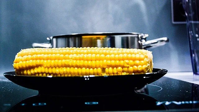 Pára nad uvařenou kukuřicí na talíři s hrncem v pozadí.