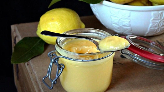 Sklenice s citronovou náplní vedle čerstvých citrónů.