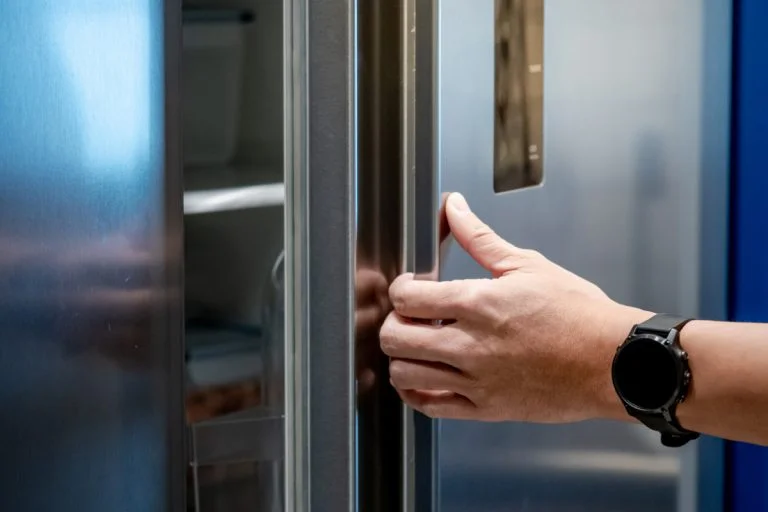 Ruka otevírá dveře chladničky s viditelnými policemi uvnitř.