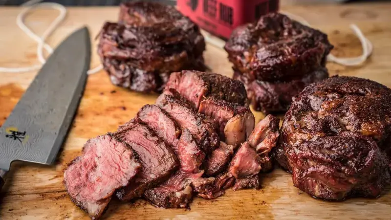 Nakrájený pečený hovězí steak na dřevěném prknu s nožem.
