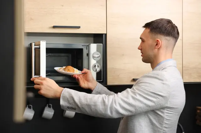 Muž vkládá jídlo do mikrovlnné trouby v kuchyni.