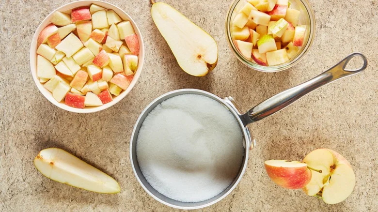 Ingredience pro kompot: jablka, hrušky a cukr v hrnci.