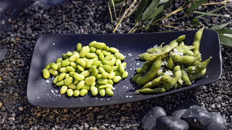 Černý talíř s uzenými fazolemi edamame v lupenech i bez nich.