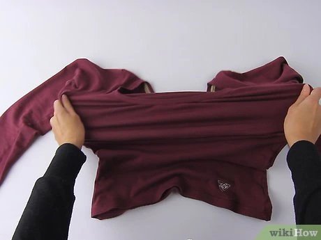Ruce natahují červené tričko na bílém podkladu.