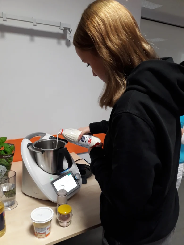 Člověk nalévá mléko do kuchyňského robotu s ingrediencemi.