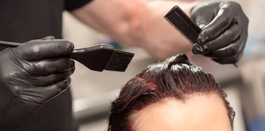Stylista nanáší barvu na vlasy štětcem s rukavicemi.