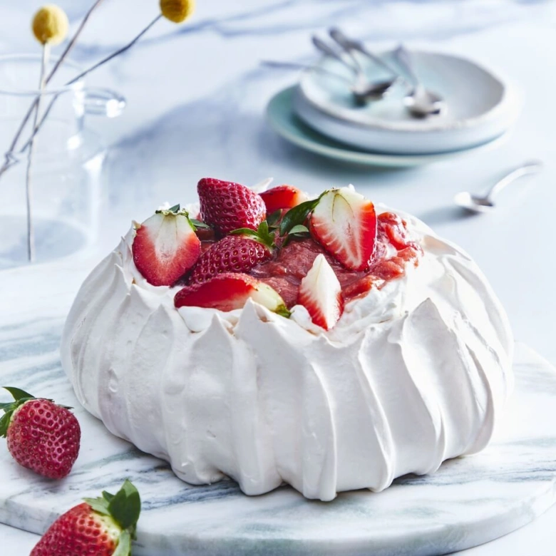 Zdobená jahodová pavlova s čerstvými jahodami na mramorovém podkladu.