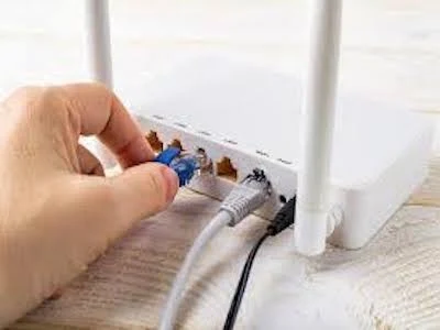 Ruka zapojuje síťový kabel do portu na bílém Wi-Fi routru.