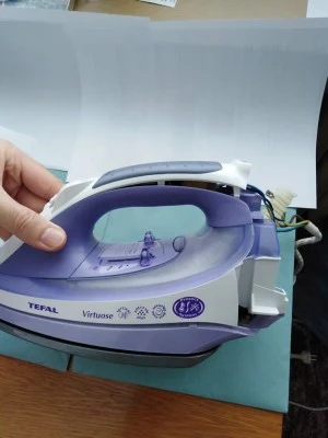 Ruka drží fialovou žehličku značky Tefal na krabici.