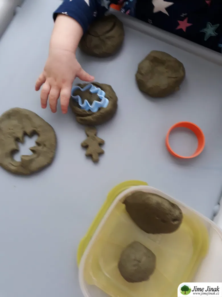 Dítě tvaruje domácí plastelínu pomocí formičky na stůl.