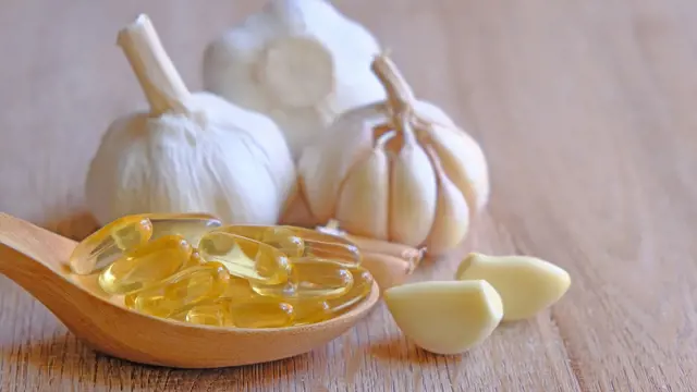 Hlava česneku se stroužky a olejem v lžíci na dřevěném povrchu.