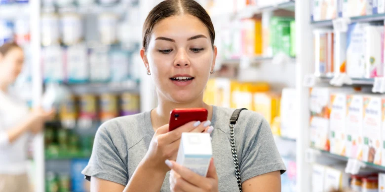 Žena v lékárně čte na mobilu vedle krému Desitin