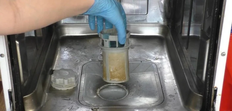 Ruční vyjímání špinavého filtru z myčky při údržbě.