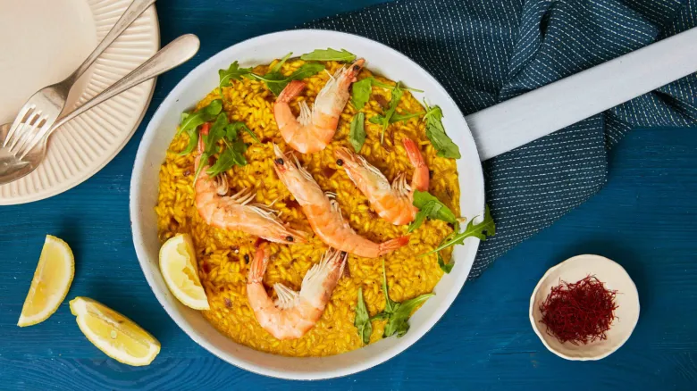 Paella s šafránem a krevety na modrém stole.