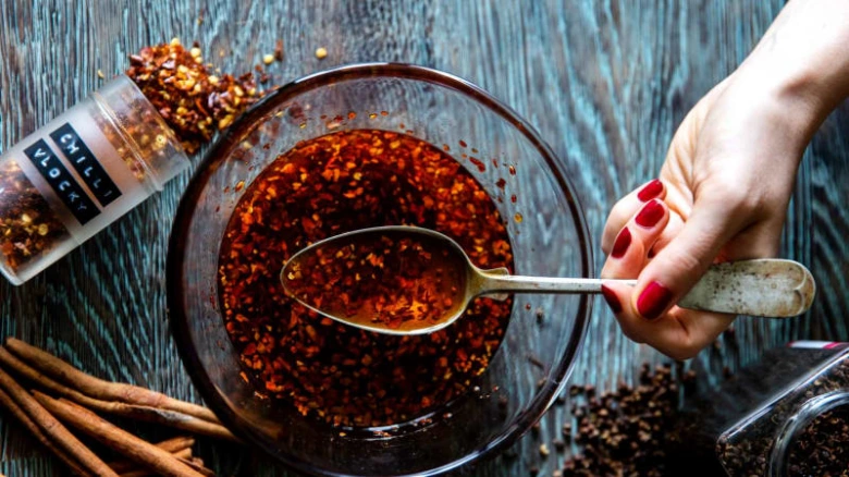 Ruka drží lžičku s chilli olejem v míse plné pepře.