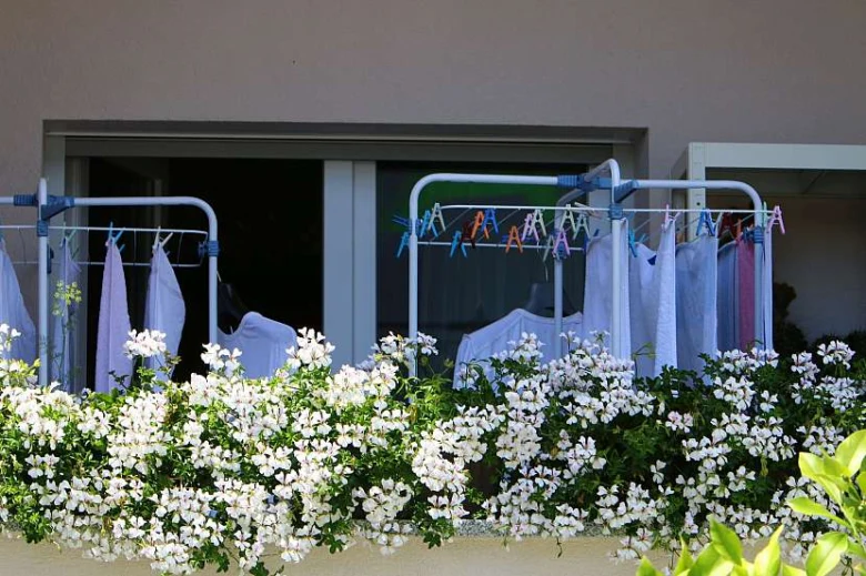 Balkon s bílými květinami a domácí sušičkou prádla.