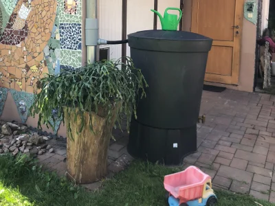 Černá nádrž na dešťovou vodu s rostlinami venku.