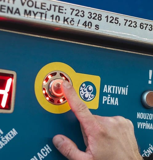 Ruka tlačí na knoflík aktivující pěnu v samoobslužné myčce.