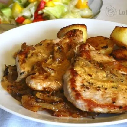 Zapečené vepřové kotlety s bramborami a cibulí na talíři.