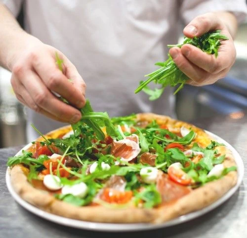 Kuchař přidává čerstvou zeleninu na pizzu.