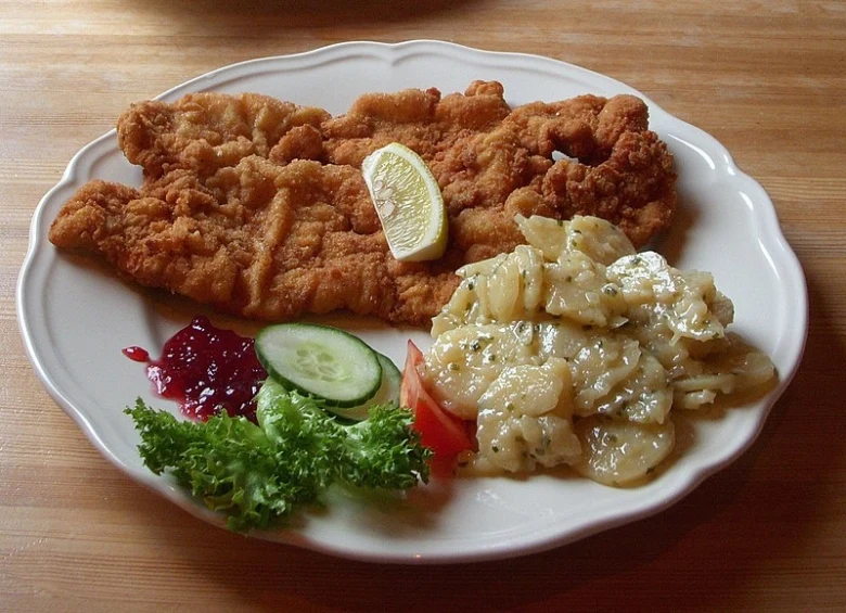 Zlatavý smažený řízek s bramborovým salátem a okurkou na talíři.
