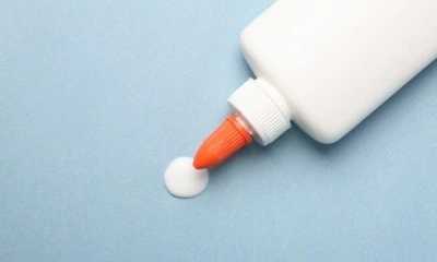 Bílá lepidlo s oranžovou tryskou vypouští kapku na modrý povrch.