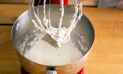Bílá zakysaná smetana se šleha v kuchyňském mixéru.