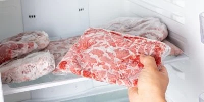 Ruka drží balenou vepřovou panenku ve skříni mrazicího boxu.