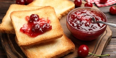 Třešňový džem s peckami na toastu vedle misky.