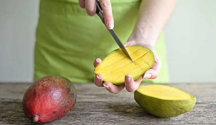 Člověk krájí mango na kostičky po očištění.