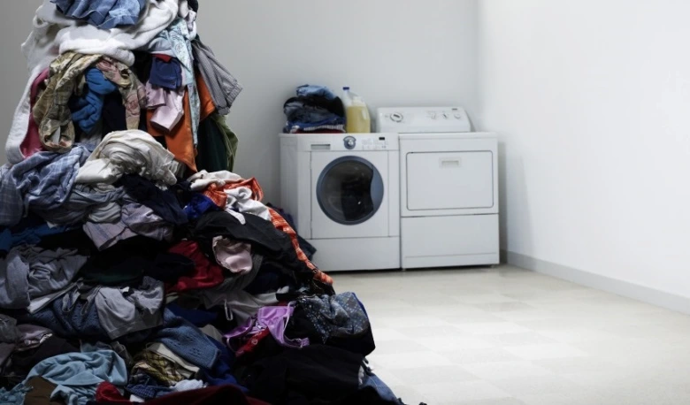 Hromada špinavého prádla před pračkou v bílé místnosti.