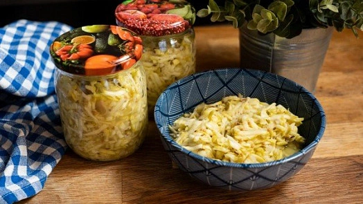 Nakládané zelí v misce vedle sklenic s nakládkou.